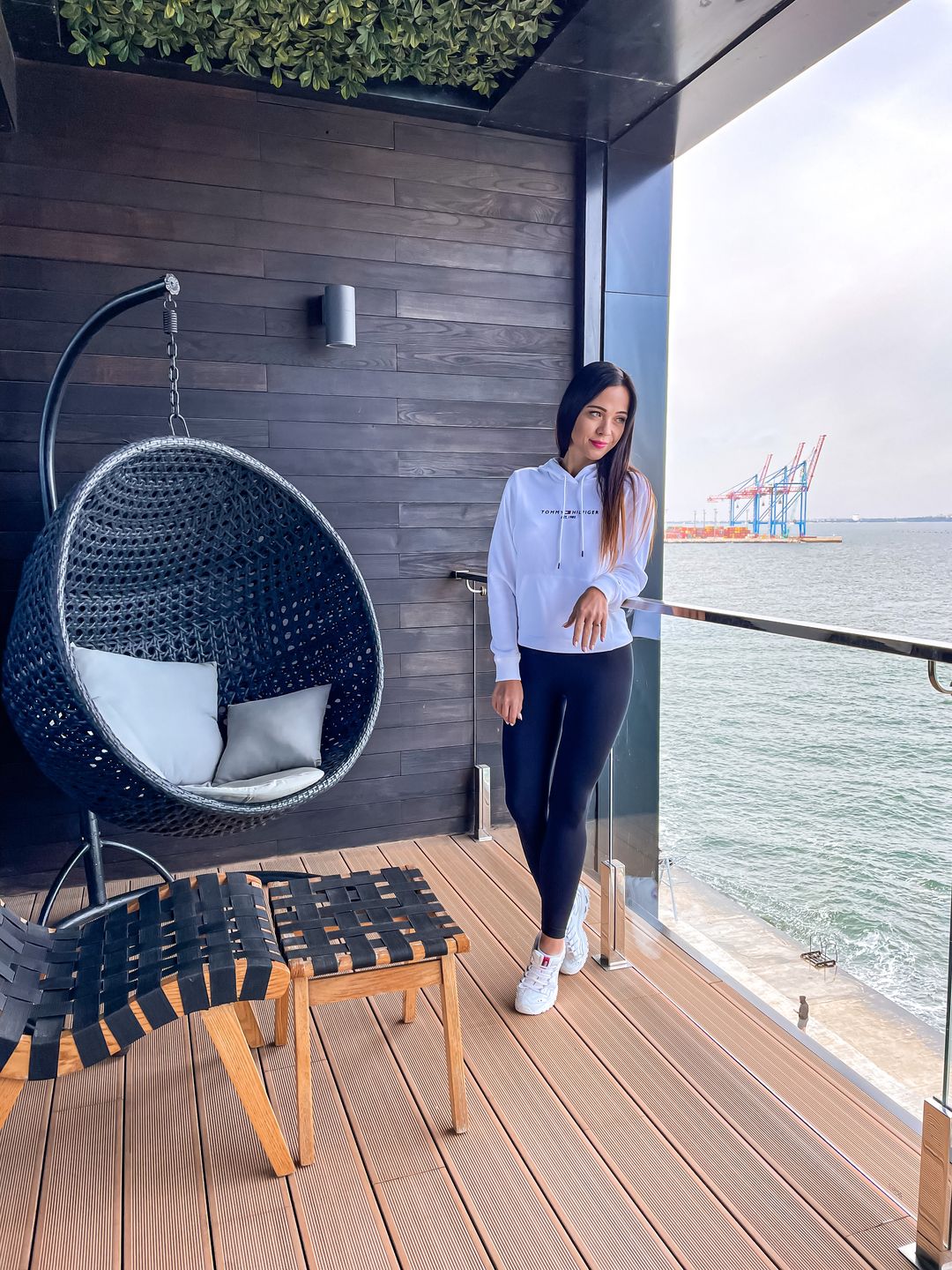 Karolina standing on a suite balcony with a hanging chair, overlooking the sea