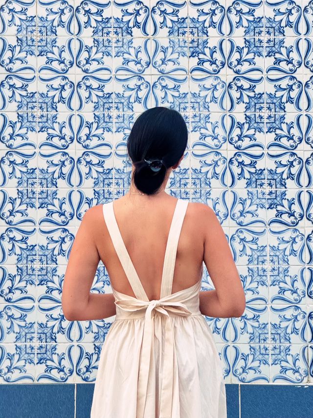 Woman in a white backless dress standing before a wall of blue and white Portuguese tiles