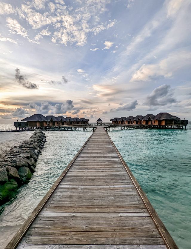 Wooden boardwalk leading to overwater villas under a dramatic sky in the Maldives